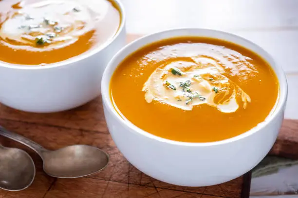 Soupe crémeuse de potiron et carottes au curry, garnie de graines de courge torréfiées dans un bol rustique